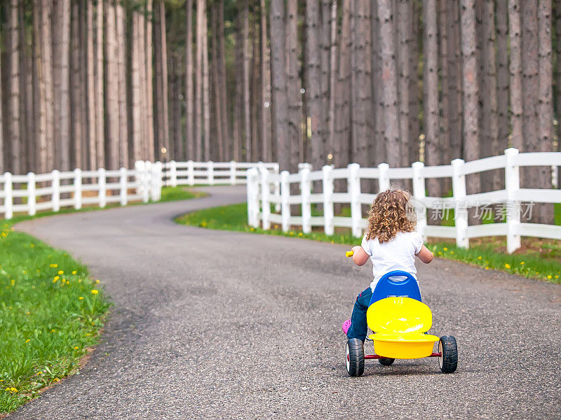 小女孩骑着三轮车走在乡间车道上