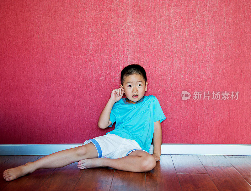 小男孩靠墙坐在地板上
