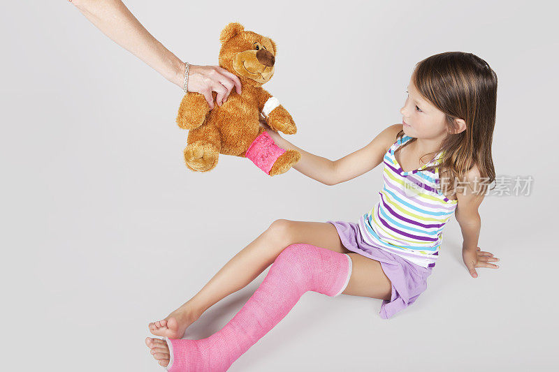 玩具熊和孩子的腿上有粉红色的石膏