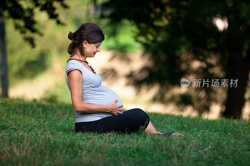 一个孕妇抱着肚子坐在草地上