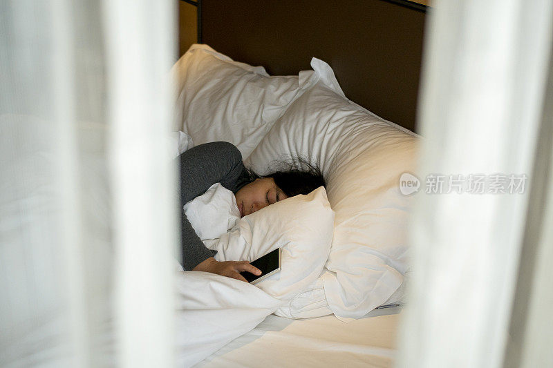 女孩睡在床上，手里拿着手机