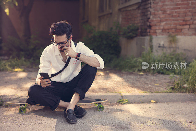 帅气的年轻人坐在长板上玩手机
