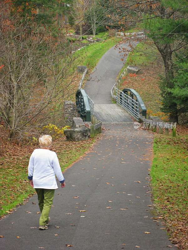金发50岁以上的女人走在自行车道上，秋天