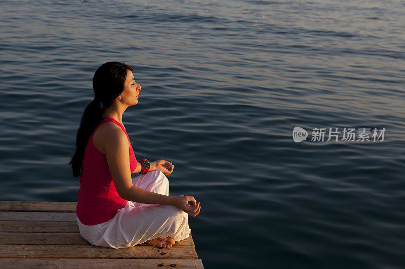 一个女人坐在湖边的码头边莲花姿势沉思