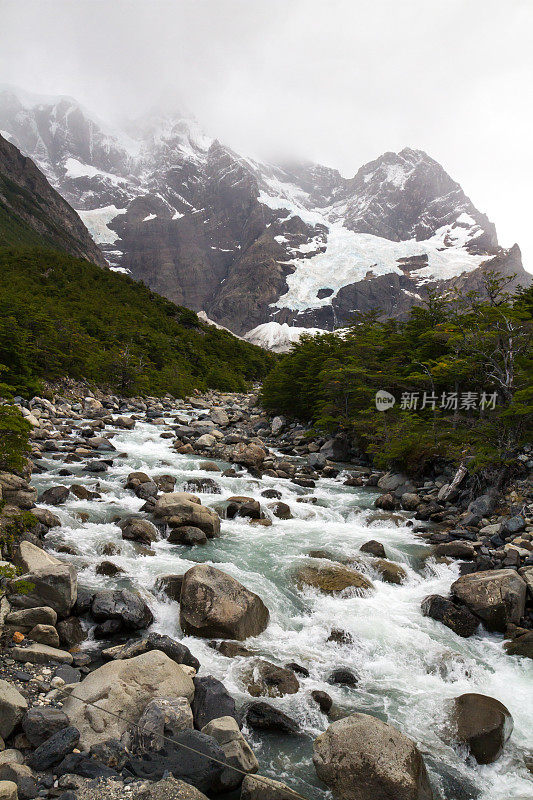 在南美洲智利巴塔哥尼亚安第斯山脉的巴塔哥尼亚地区，一条阿尔卑斯溪流强劲地流动着，背景是冰川