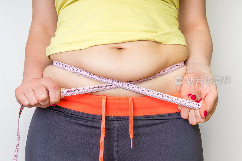 超重妇女用卷尺量肚子上的脂肪
