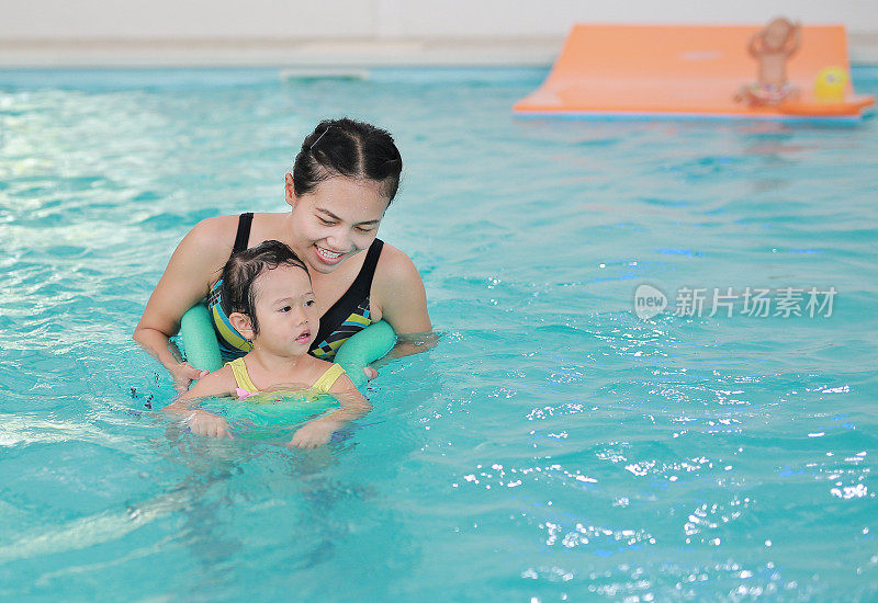 妈妈和孩子在游泳池里游泳。快乐的年轻女子教她的女儿游泳。