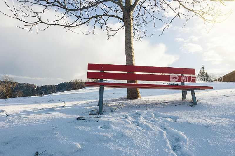 白雪覆盖的红色长凳前的冬季景观上有雪的痕迹