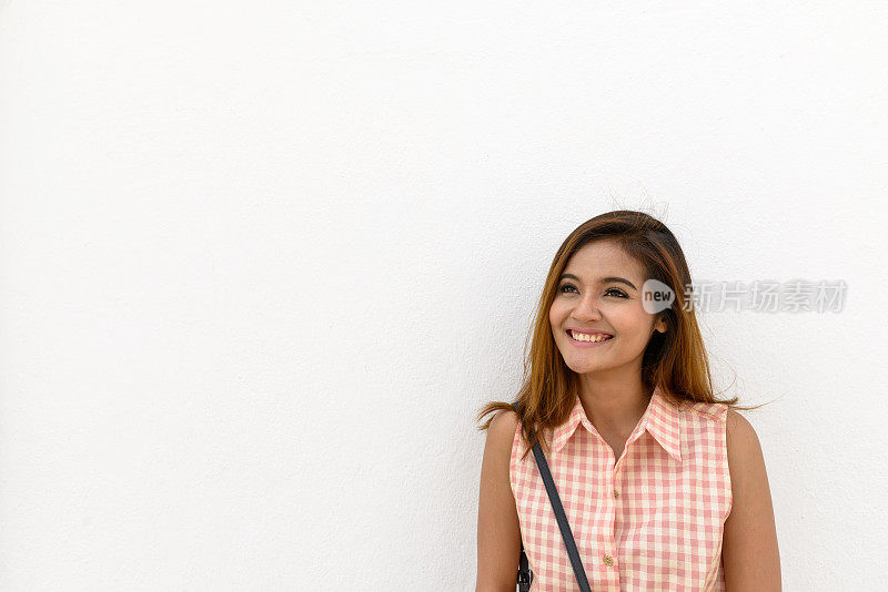 年轻美丽的亚洲女游客靠在白色的混凝土墙上