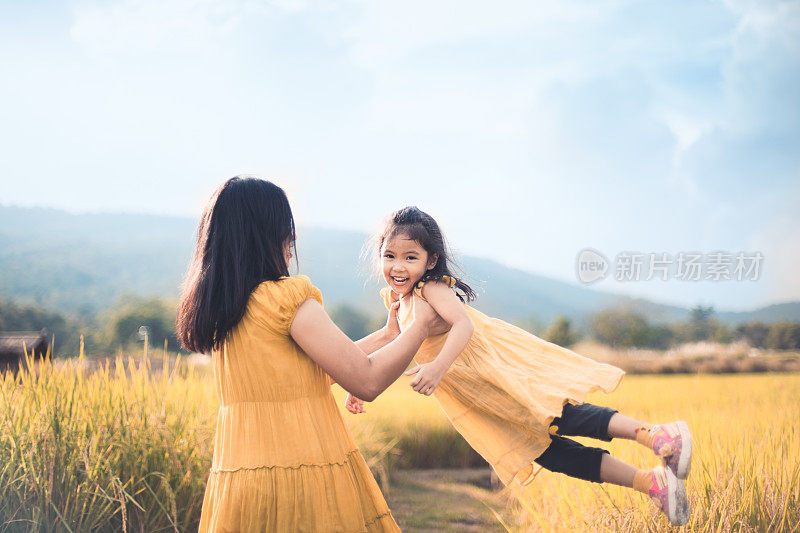 可爱的亚洲女孩微笑和有趣的母亲抱着她的孩子和旋转