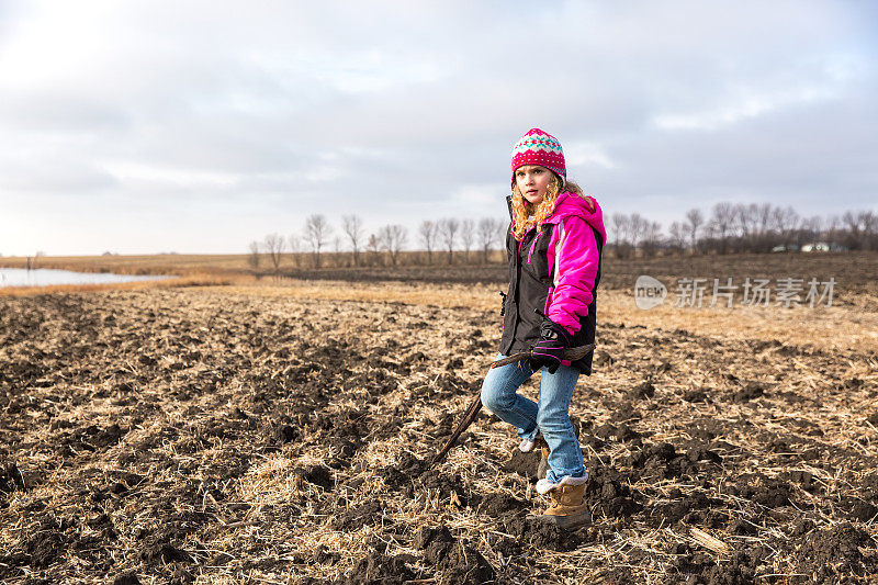 一个年轻的女孩在秋天走过犁过的大豆田