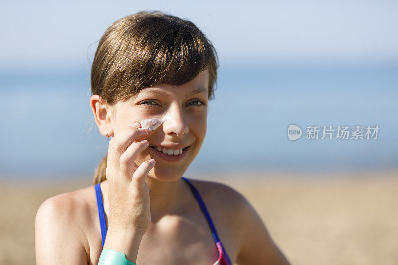 美丽的年轻女孩在海滩上使用防晒霜