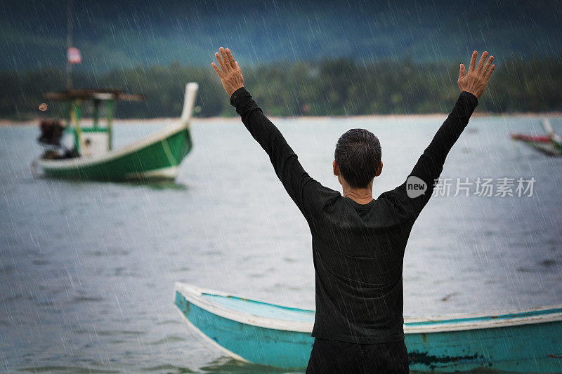 一名男子在大雨中高举双手站在岸边。