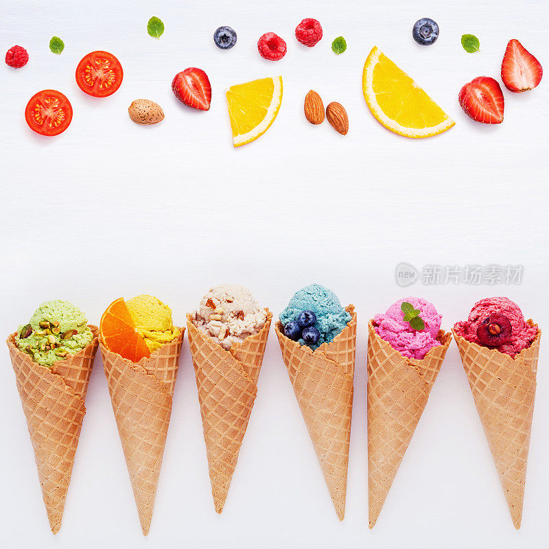 各种口味的冰淇淋圆锥蓝莓，草莓，开心果，杏仁，橙子和樱桃设置在白色的木制背景。夏季和甜蜜的菜单概念。