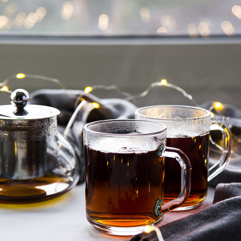 窗边的透明茶壶和杯子里装着红茶。冬天的概念