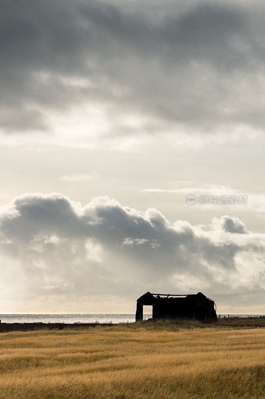 冰岛一片金色草地上的废墟剪影，乌云笼罩