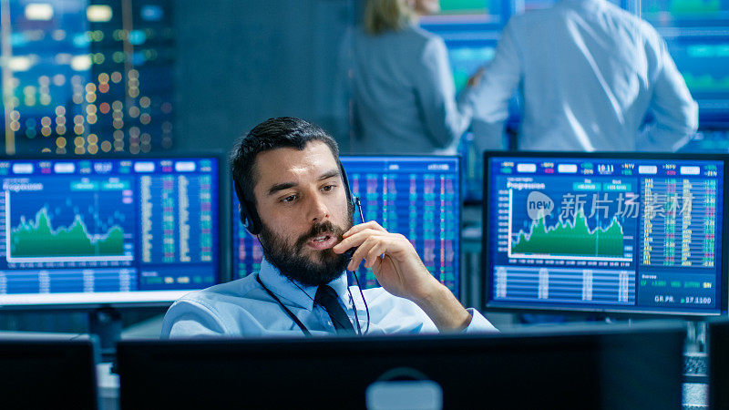证券交易所交易员通过耳机与大客户达成交易。他与其他经纪人合作，周围都是屏幕上显示图形和股票号码的计算机。