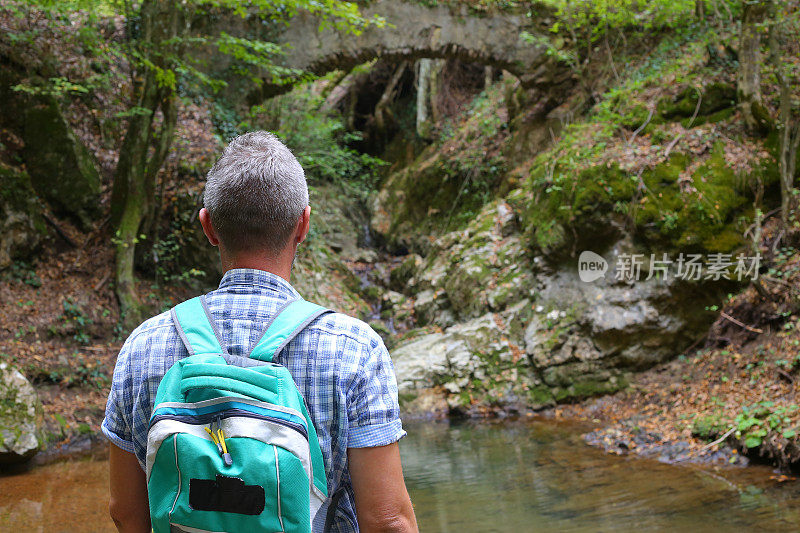 成年男子徒步旅行在美丽的自然景观与小溪流在森林和老废弃的石桥上面