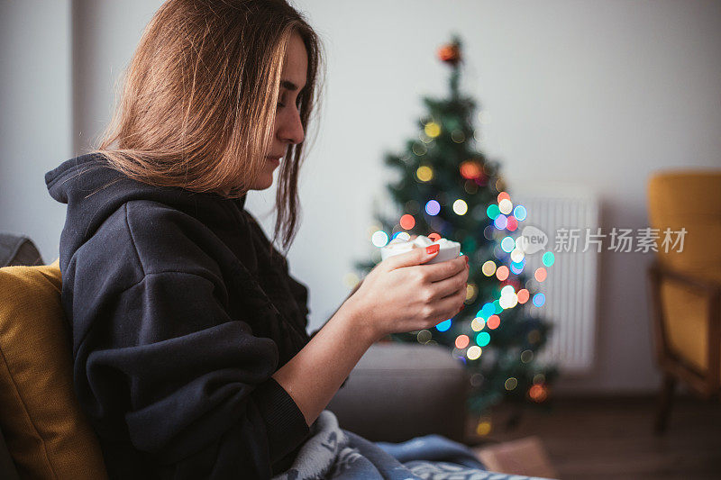 年轻女子在圣诞树旁喝着热巧克力