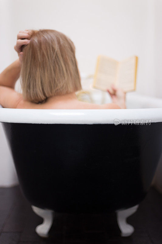 女人洗澡和阅读在古董爪足浴缸