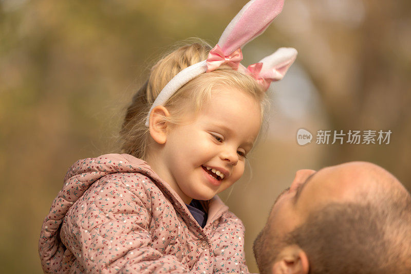 可爱的小女孩兔耳朵微笑时，她的父亲抱着她