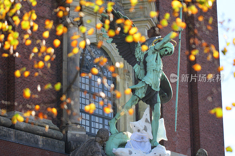古老的古董绿色金属方丹圣迈克尔雕像与黄橙色花bogae在基督教教堂前德国汉堡