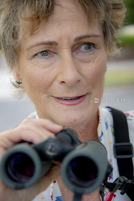 成熟的女人用双筒望远镜观鸟。