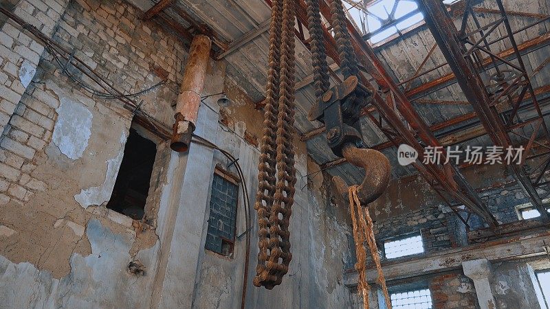 在一个废弃的工厂里，生锈的大铁钩用链条吊在天花板上