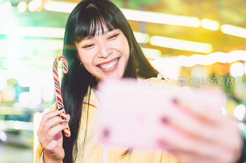 亚洲女孩在游乐园与手机自拍-快乐的女人与新的趋势智能手机应用程序-青年千禧一代和社交媒体成瘾的概念