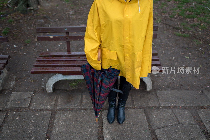 穿着黄色雨衣的年轻女子在公园里度过雨天