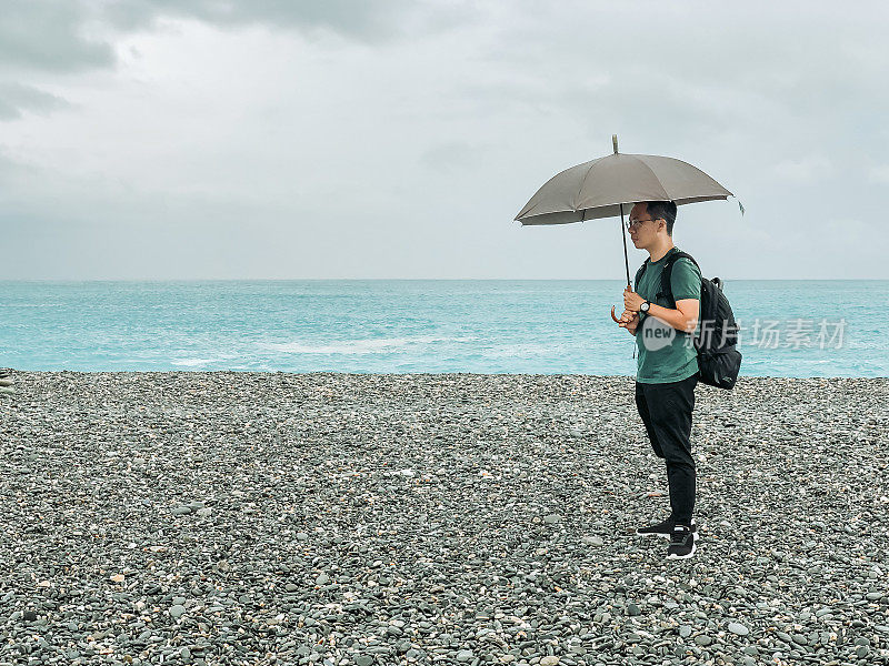 一名亚裔中国男游客在海滩上撑着伞