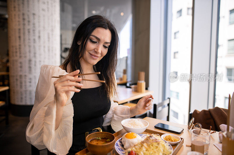 白人妇女吃日本食物“汉堡牛排”午餐，使用筷子