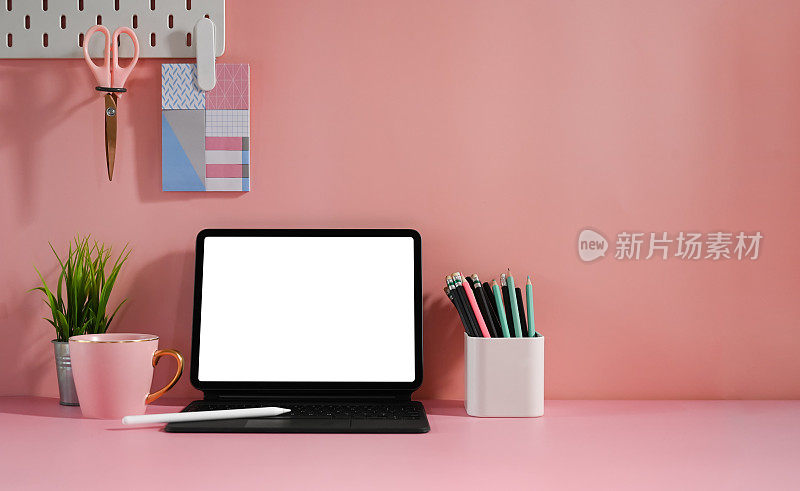 一个白色空白屏幕的平板电脑放在一个妇女的桌子上，周围摆满了各种设备。