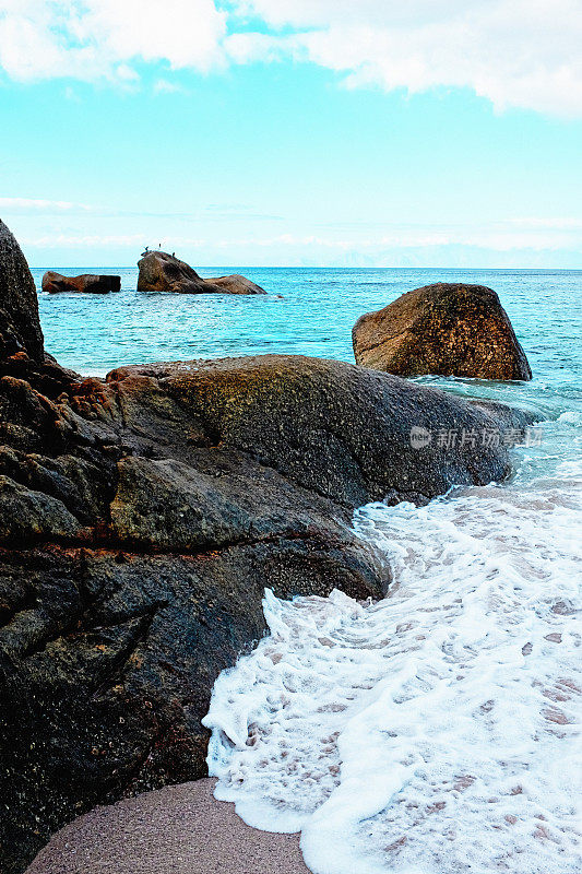 在美丽的海岸线上，泡沫状的海浪拍打着海滩边的岩石