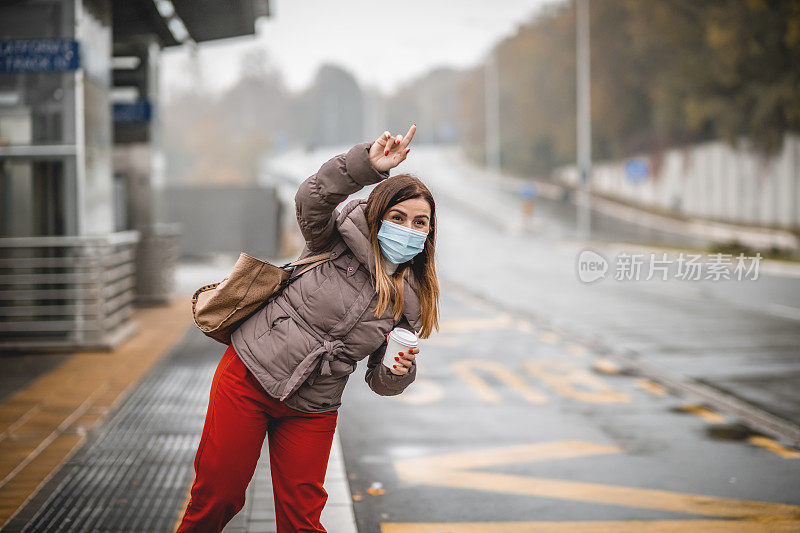 年轻女子戴着防护口罩去上班。在公共汽车站停出租车