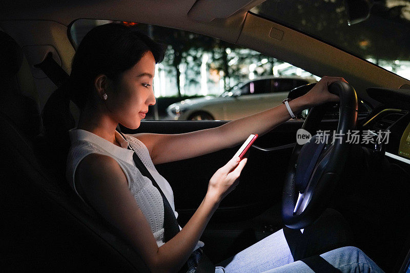 坐在汽车驾驶座上使用手机的年轻女子