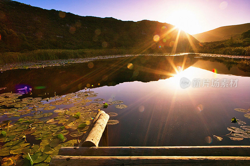 夕阳倒映在平静的湖面上，前景是木制的防波堤