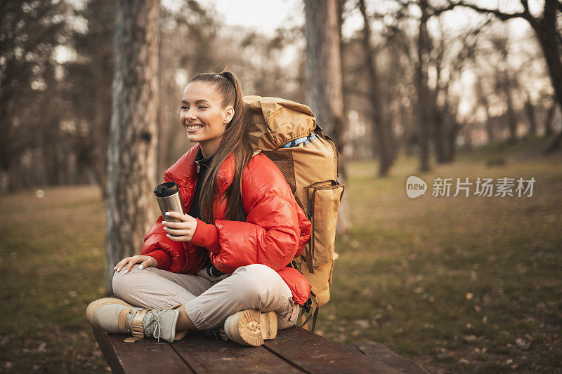 美丽的年轻女子喝着咖啡，在山间徒步旅行时休息一下