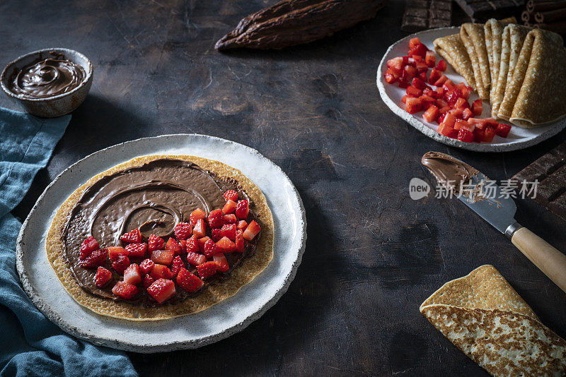 可丽饼素食Crêpes与可可奶油巧克力涂抹和草莓在深色木材的背景
