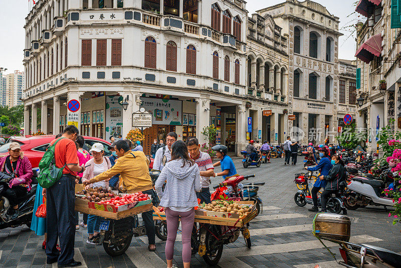游客在水巷的街头小吃摊上购买水果，这里有古老的殖民建筑和海南老城的居民