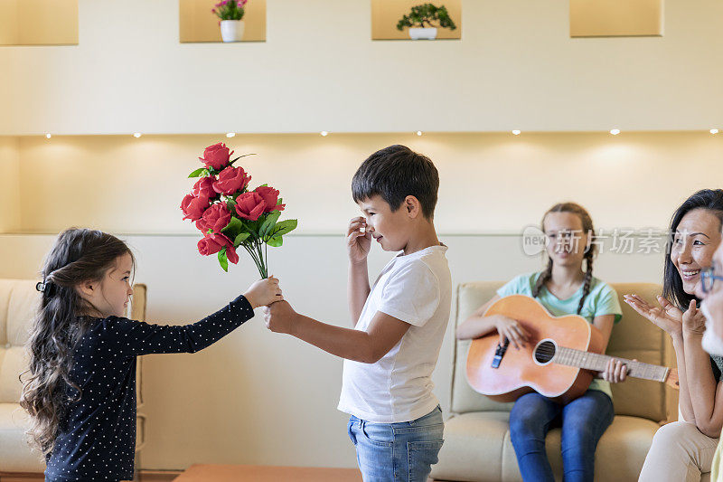 一个小男孩送给他可爱的妹妹一朵红玫瑰作为生日礼物。