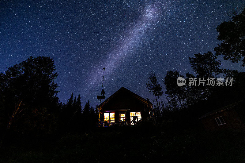 夜空和银河大自然在森林中美丽的小房子或小屋后面的全景图