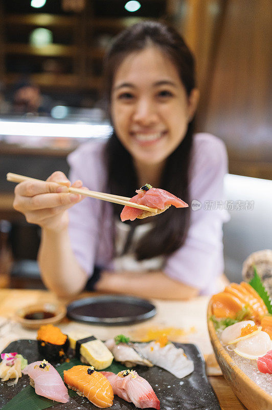 Z一代年轻的亚洲女性享受着豪华的日本料理与什锦寿司，海鲜，牡蛎，生鱼片在餐厅的餐桌上新鲜供应。亚洲美食和食物。外出就餐的生活方式