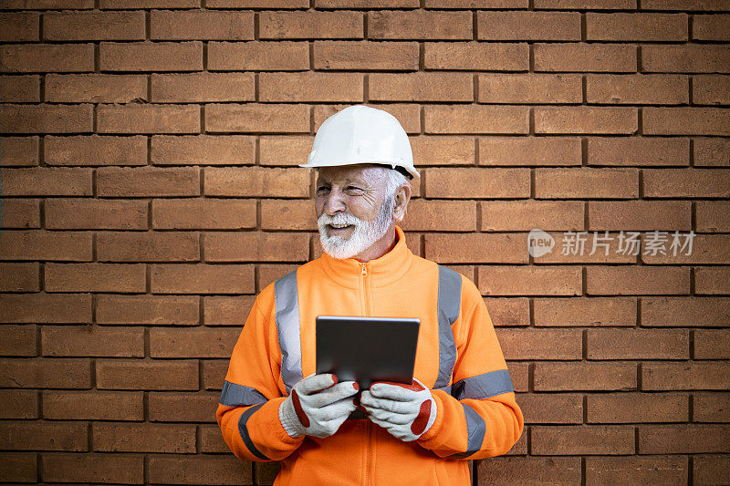 一名经验丰富的建筑工人戴着安全帽和安全设备站在工地的砖墙旁。