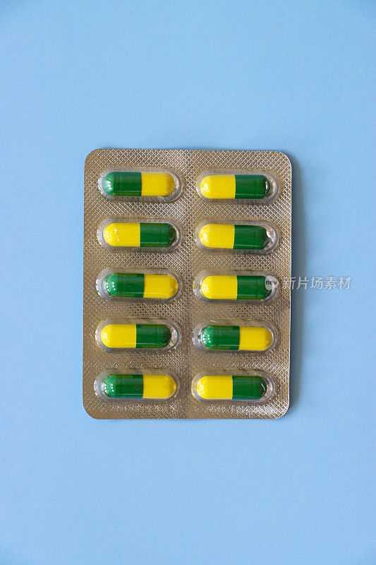 特写图像个人银背制药片剂泡罩包，一排排黄色和绿色明胶胶囊药物可见通过透明塑料口袋，蓝色背景，上升的观点