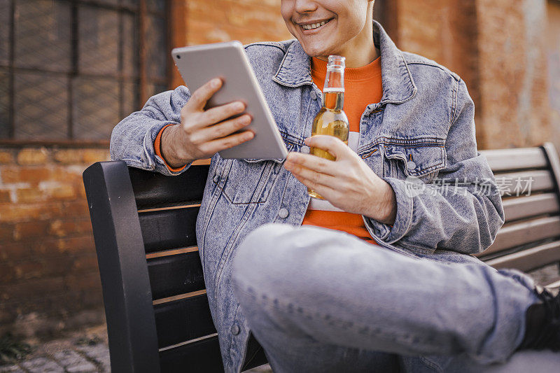 嬉皮士年轻人在公园长椅上用数码平板电脑喝啤酒