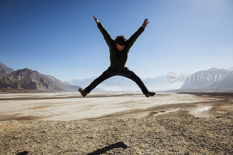 一名男子在巴基斯坦喀喇昆仑山脉的风景中跳跃