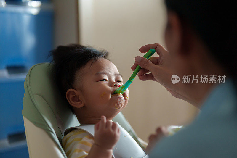 坐在高椅子上的亚洲小男孩正在被妈妈喂食。