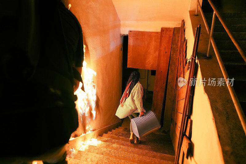 勇敢的消防员从着火的大楼里走下楼梯，将获救的女孩抱在怀里。明火，背景中有一名消防员。