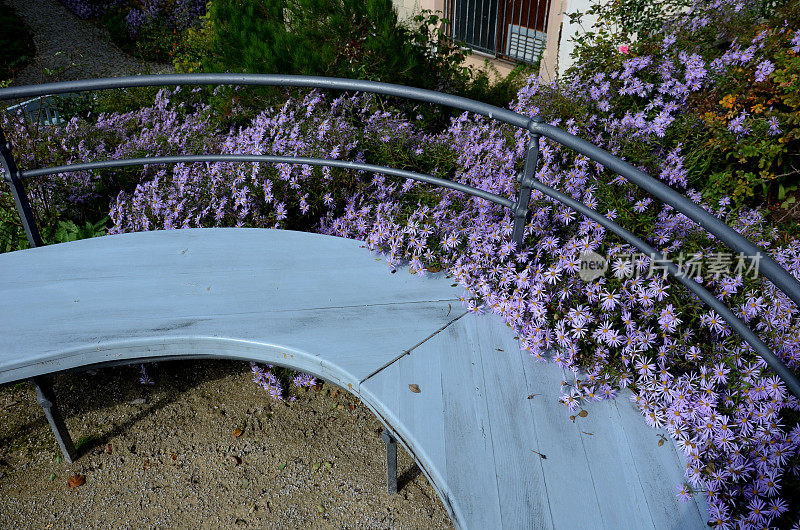 用纯浇铸混凝土制成的挡土墙后面开着紫色的花，墙的边缘是带黑绳的金属栅栏，挡住花坛的入口